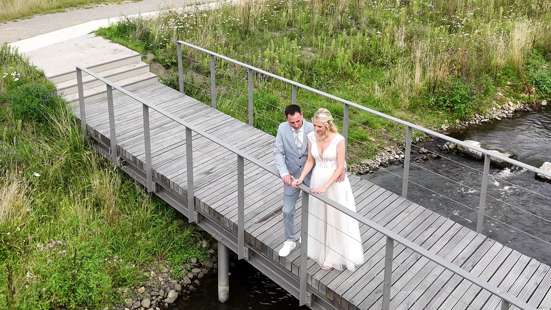 Brautpaar auf einer Holzbrücke über einem Bach, von oben fotografiert