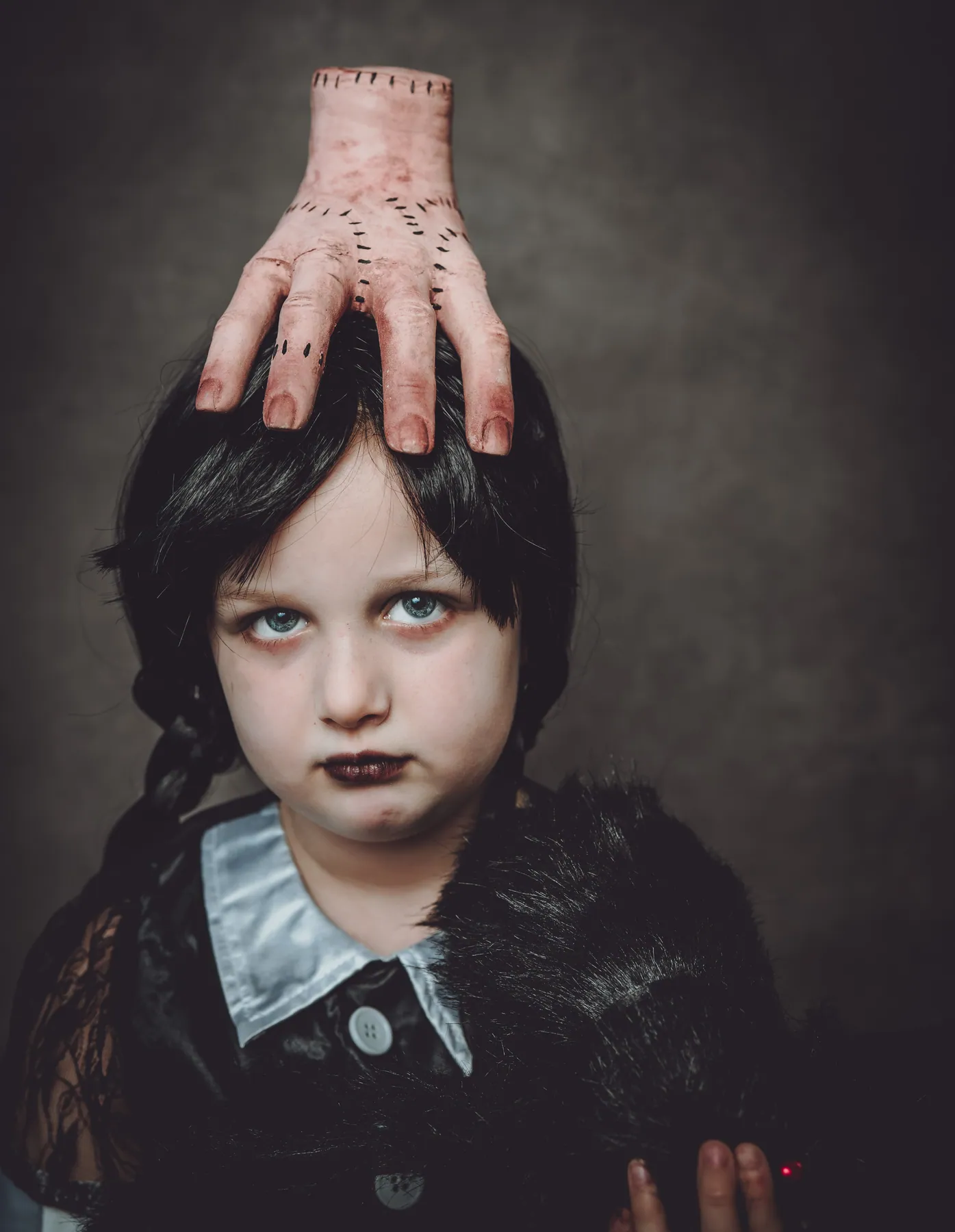Mädchen im Wednesday-Kostüm, eine Hand auf dem Kopf