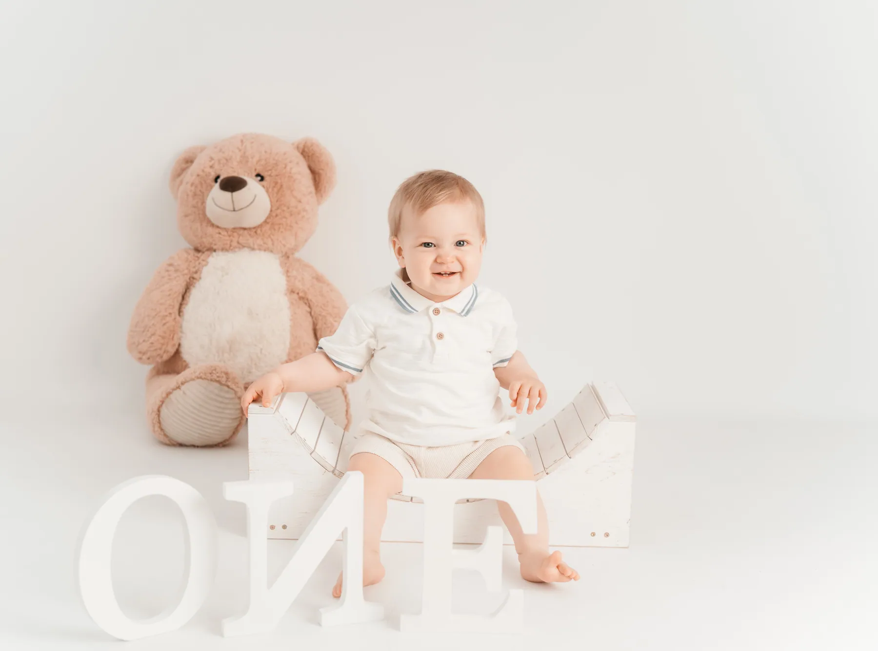 Kind mit Teddy im hellen Studio, davor die Buchstaben ONE