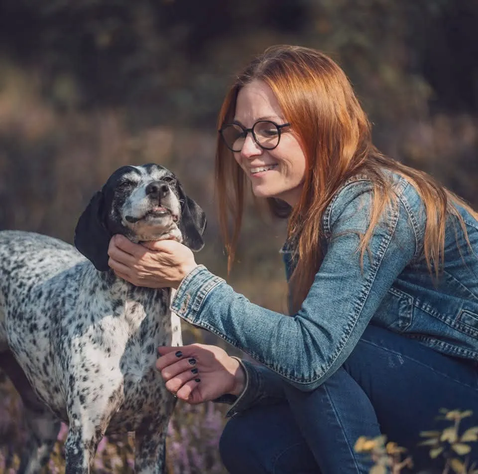 Patricia lachend mit einem gefleckten Hund in der Heide