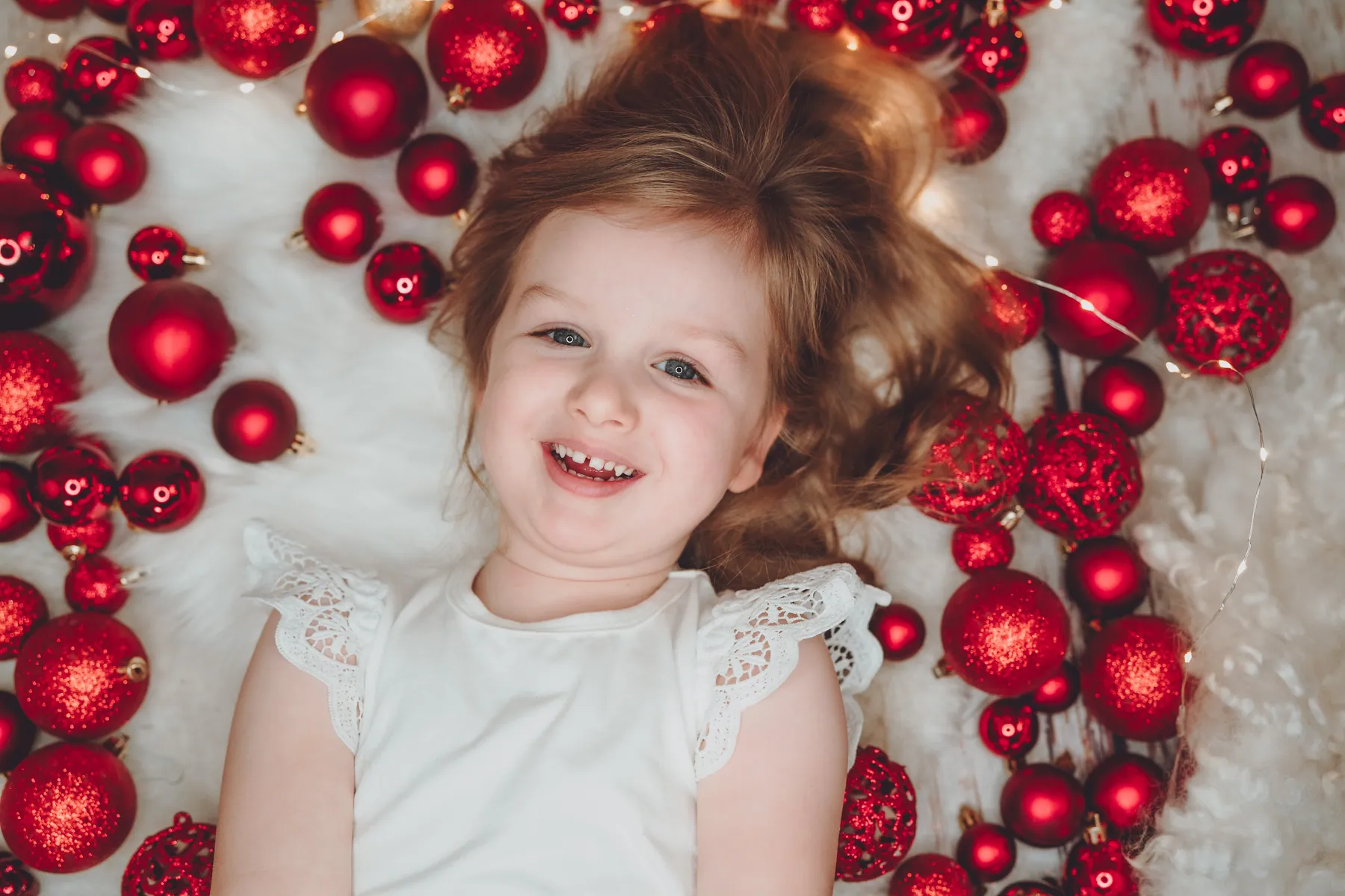 Mädchen liegt zwischen roten Weihnachtskugeln